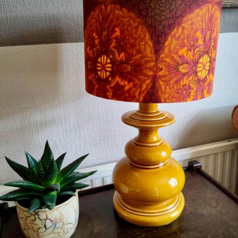 May include: A vintage table lamp with a yellow ceramic base and a patterned orange and brown lampshade.