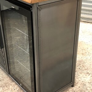 Pode incluir: Um m&oacute;vel bar com tampo de madeira natural e estrutura de metal cinza-escuro. A unidade inclui um frigor&iacute;fico embutido com porta de vidro, com a marca Baridi vis&iacute;vel na moldura. O painel lateral &eacute; feito de metal s&oacute;lido cinza-escuro.