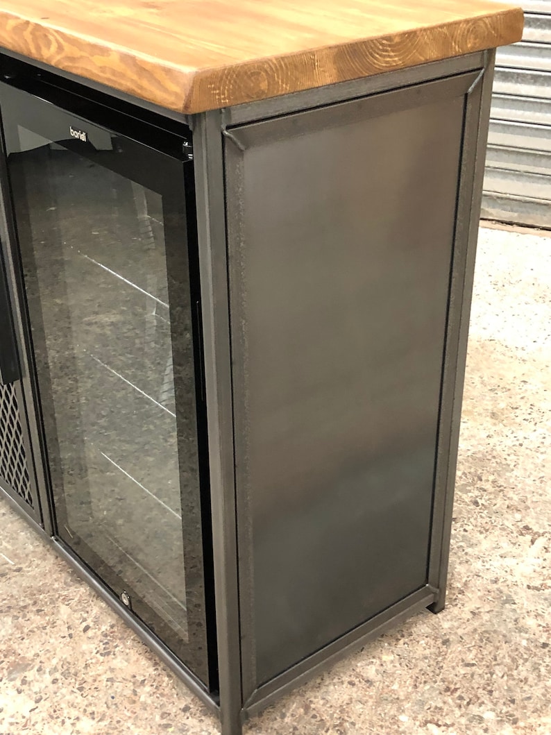 Pode incluir: Um m&oacute;vel bar com tampo de madeira natural e estrutura de metal cinza-escuro. A unidade inclui um frigor&iacute;fico embutido com porta de vidro, com a marca Baridi vis&iacute;vel na moldura. O painel lateral &eacute; feito de metal s&oacute;lido cinza-escuro.