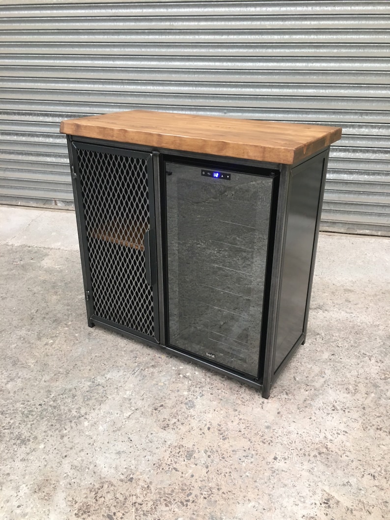 Op de afbeelding: Een zwarte metalen kast met een houten blad en een ingebouwde wijnkoeler. De kast heeft een draadgaasdeur aan de linkerkant en een glazen deur aan de rechterkant. De wijnkoeler heeft een digitaal display en een glazen deur.