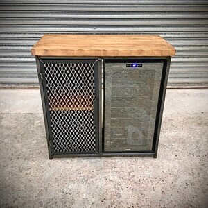 Op de afbeelding: Een zwarte metalen kast met een houten blad en een glazen deur wijnkoeler. De kast heeft een draadgaasdeur aan de linkerkant.