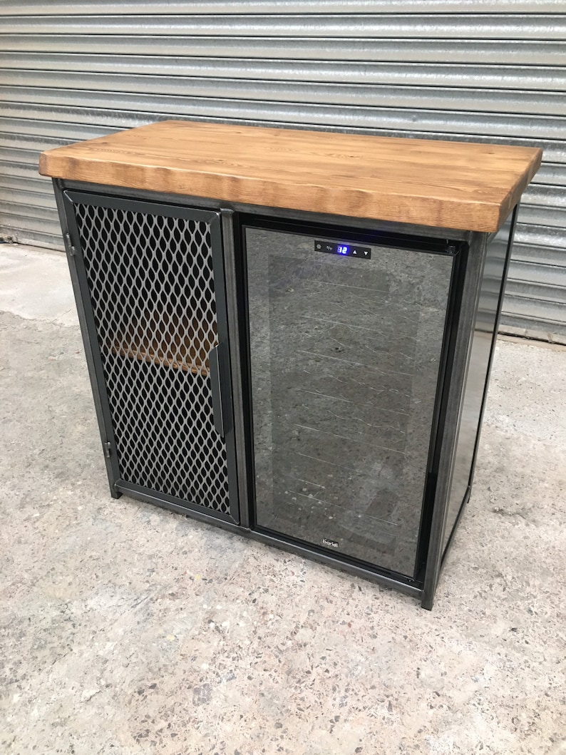 Op de afbeelding: Een zwarte metalen kast met een houten blad en een ingebouwde wijnkoeler. De kast heeft een draadgaasdeur aan de linkerkant en een glazen deur aan de rechterkant. De wijnkoeler heeft een digitaal display en een temperatuurregelaar.