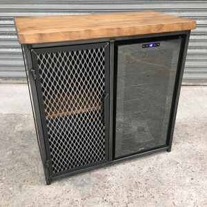 Op de afbeelding: Een zwarte metalen kast met een houten blad en een glazen deur wijnkoeler. De kast heeft een draadgaasdeur aan de linkerkant.