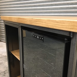 May include: A black metal cabinet with a wood top and a glass door. The cabinet has a built-in wine cooler with a digital display that shows the temperature.