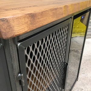Op de afbeelding: Een zwarte metalen kast met een houten bovenblad en een deur van draadgaas. De kast heeft een ingebouwde wijnkoeler met een glazen deur.