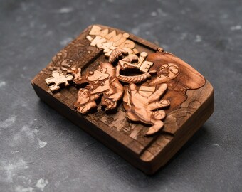 May include: A wooden box with a carved design of a cartoon character. The box is brown and has a puzzle piece on the side. The text "BANG!" is carved into the box.