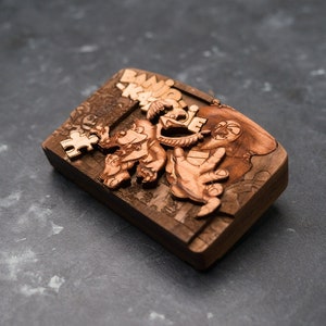 May include: A wooden box with a carved design of a cartoon character. The box is brown and has a jigsaw piece on the side. The text "BANG!" is carved into the box.