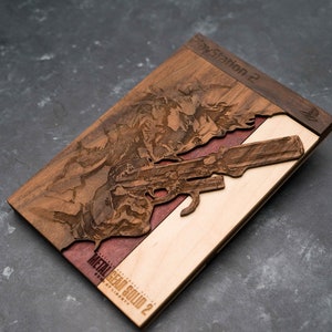 May include: A wooden game case with a laser-engraved image of a character holding a gun. The case is made of three different types of wood: walnut, maple, and cherry. The text "PlayStation 2" and "Metal Gear Solid 2" is engraved on the case.