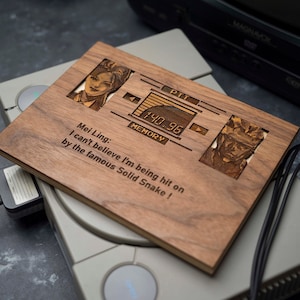 May include: A wooden plaque with a laser-engraved image of a video game character, Solid Snake, from the Metal Gear Solid video game. The plaque also features a quote from the game, "Mei Ling: I can't believe I'm being hit on by the famous Solid Snake!"