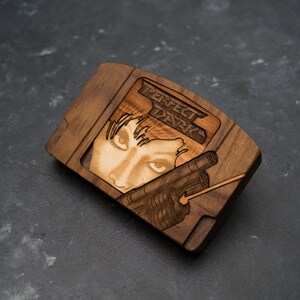 May include: A wooden replica of a Nintendo 64 game cartridge featuring the cover art for the game "Perfect Dark". The cartridge is made of dark wood and features a laser-engraved image of the game's protagonist, Joanna Dark, holding a gun.