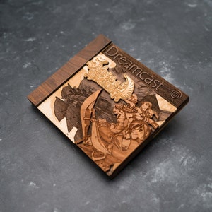 May include: A wooden Dreamcast game case with a laser-engraved image of characters from the game Skies of Arcadia. The case is made of dark wood with a light wood inlay.