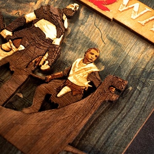 Pode incluir: Uma pe&ccedil;a de arte de parede de madeira que representa duas figuras do videojogo God of War. As figuras s&atilde;o esculpidas em relevo e pintadas em tons de castanho e bege. O fundo &eacute; uma textura de madeira castanho escuro e azul. A palavra "WAR" &eacute; esculpida em relevo numa pe&ccedil;a de madeira separada e pintada em branco.