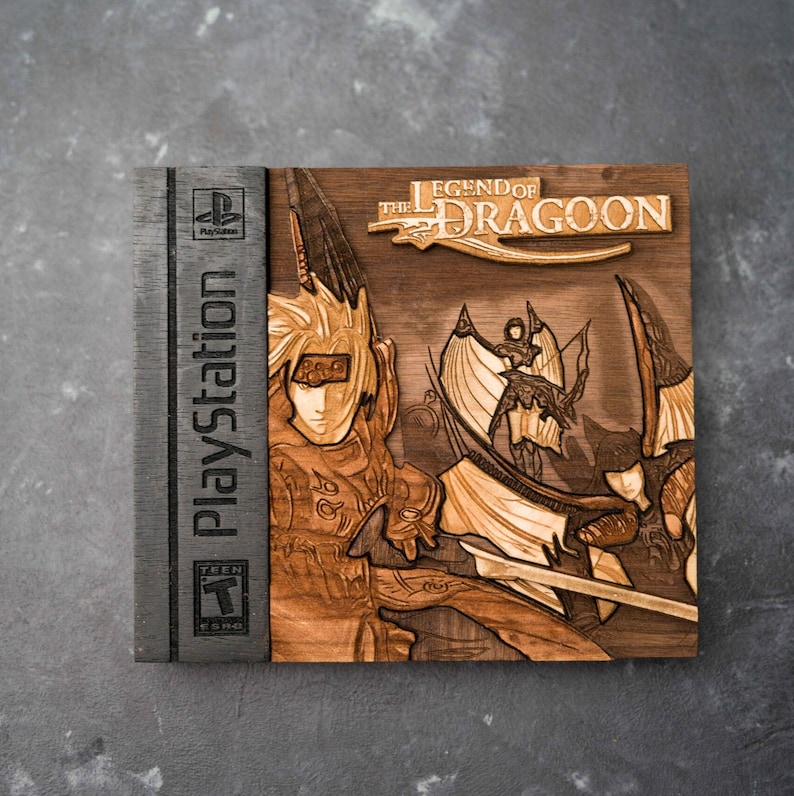 May include: A wooden laser-cut replica of the PlayStation game case for The Legend of Dragoon. The case features a brown wood background with a detailed image of the game's main character, a young man with blonde hair and a blue bandana, holding a sword. The game title is printed in white on a black banner.