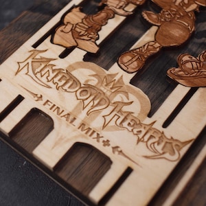Puede incluir: Una caja de madera con un dise&ntilde;o grabado con l&aacute;ser que presenta el logotipo y los personajes de Kingdom Hearts. La caja est&aacute; hecha de dos tipos diferentes de madera, una clara y otra oscura. El texto "FINAL MIX" est&aacute; grabado debajo del logotipo.