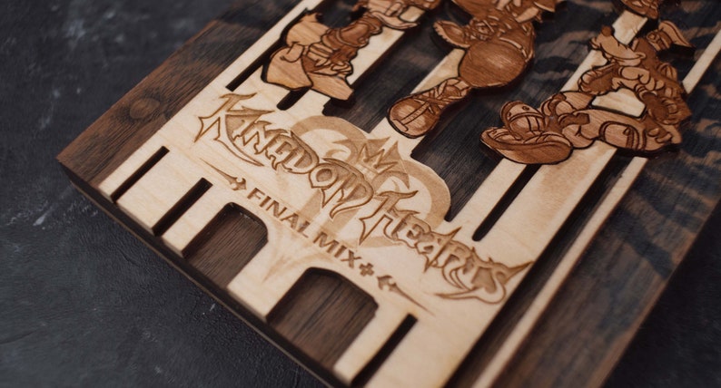Puede incluir: Una caja de madera con un dise&ntilde;o grabado con l&aacute;ser que presenta el logotipo y los personajes de Kingdom Hearts. La caja est&aacute; hecha de dos tipos diferentes de madera, una clara y otra oscura. El texto "FINAL MIX" est&aacute; grabado debajo del logotipo.