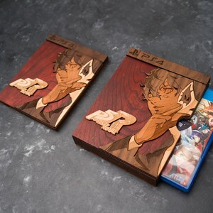 Puede incluir: Dos estuches de juego de madera con un acabado te&ntilde;ido de rojo. Los estuches presentan una imagen estilizada de una persona con cabeza de lobo. El texto "PS4" est&aacute; impreso en la parte superior de cada estuche. El estuche de la derecha tiene un disco de juego azul en su interior.