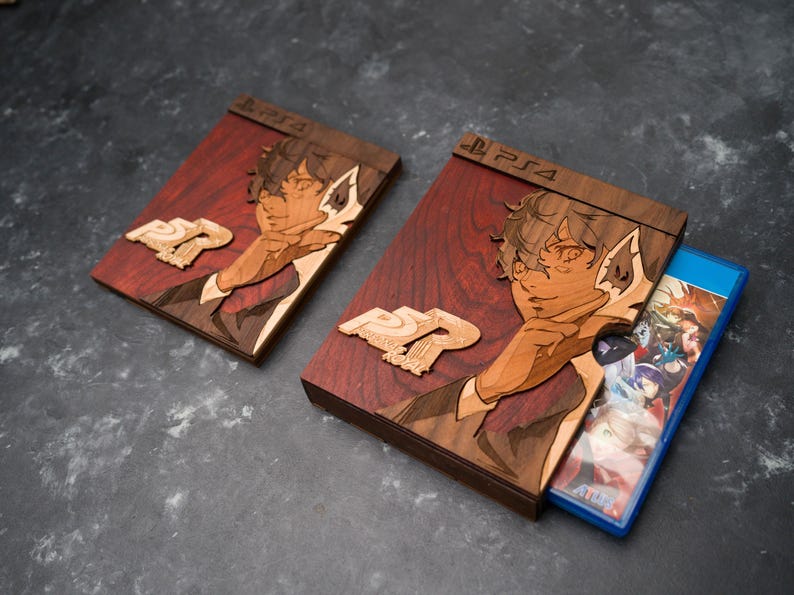 Puede incluir: Dos estuches de juego de madera con un acabado te&ntilde;ido de rojo. Los estuches presentan una imagen estilizada de una persona con cabeza de lobo. El texto "PS4" est&aacute; impreso en la parte superior de cada estuche. El estuche de la derecha tiene un disco de juego azul en su interior.