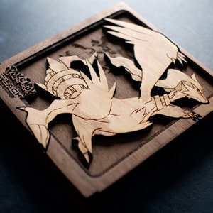 May include: A wooden plaque with a detailed laser-cut design of two mythical creatures. The plaque is dark brown with a lighter brown design. The text "Pokemon Black" is engraved in the top left corner.