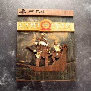 Pode incluir: Uma caixa de jogo de madeira para o jogo God of War para PlayStation 4. A caixa apresenta uma imagem queimada em madeira de Kratos e Atreus em p&eacute; em um barco. O t&iacute;tulo "God of War" est&aacute; escrito em letras douradas na parte superior da caixa.