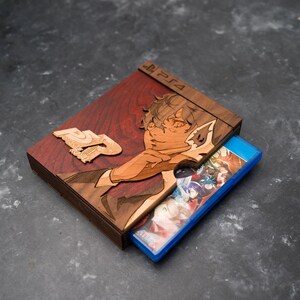 Pode incluir: Uma caixa de jogo de madeira com acabamento em madeira de gr&atilde;o vermelho. A caixa apresenta um design de corte a laser de um personagem com um disco de jogo azul no interior. A caixa tem o texto "PS4" na parte superior.