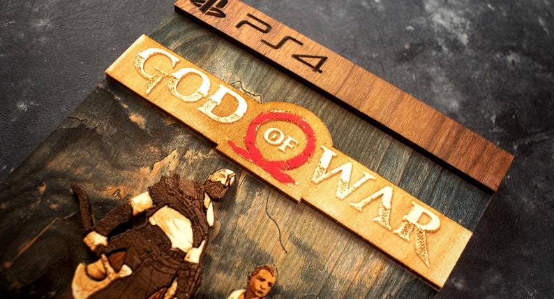 Pode incluir: Uma capa de jogo de madeira para o jogo God of War para PlayStation 4. A capa apresenta uma imagem 3D de Kratos e Atreus do jogo, juntamente com o t&iacute;tulo e o logotipo do jogo.