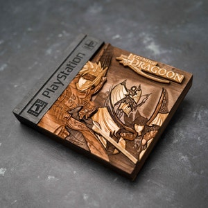 May include: A wooden PlayStation game case featuring a carved image of the characters from The Legend of Dragoon. The case is dark brown with a black PlayStation logo on the spine.