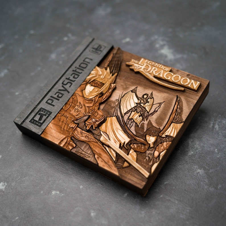 May include: A wooden PlayStation game case featuring a carved image of the characters from The Legend of Dragoon. The case is dark brown with a black PlayStation logo on the spine.
