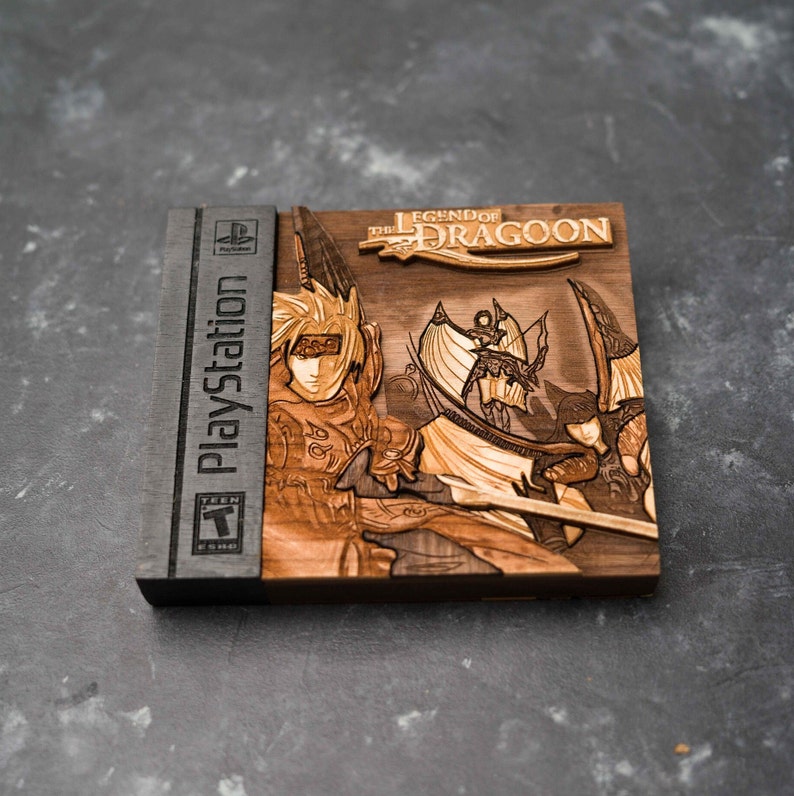 May include: A wooden laser-cut replica of a PlayStation game case for "The Legend of Dragoon". The case features a detailed image of the game's characters and title.