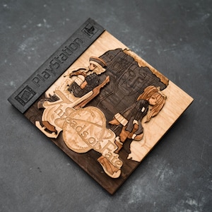 May include: A wooden PlayStation game case with a laser-cut design of two characters from the game "Threads of Fate". The case is made of dark wood with a light wood inlay. The game title is visible on the case.