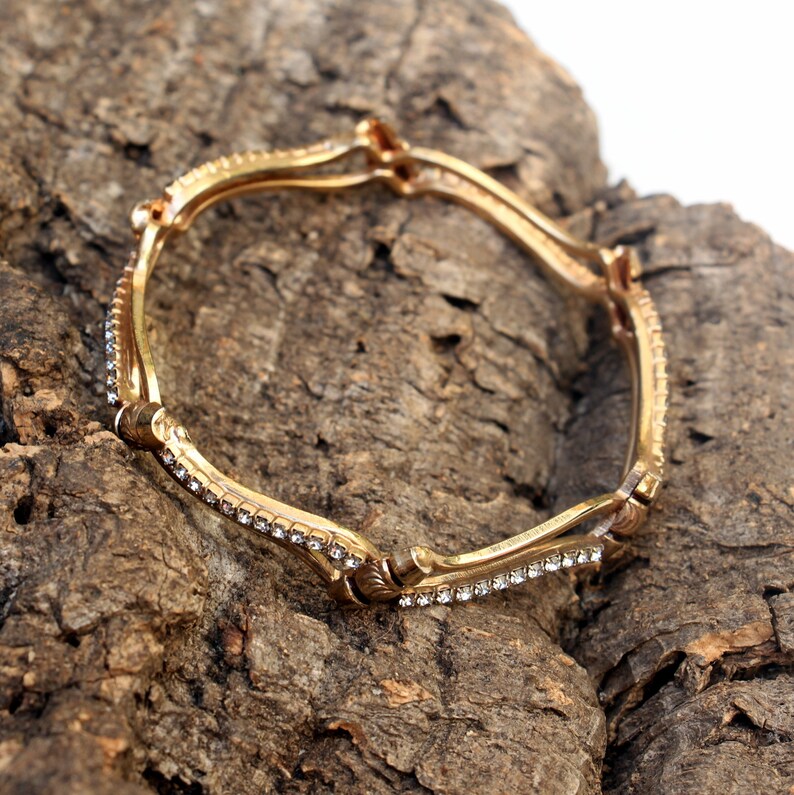 May include: A gold bangle bracelet with a wavy design and clear rhinestones.