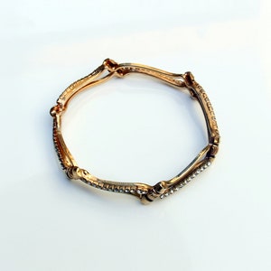 May include: A gold bangle bracelet with clear rhinestones set in a geometric pattern.