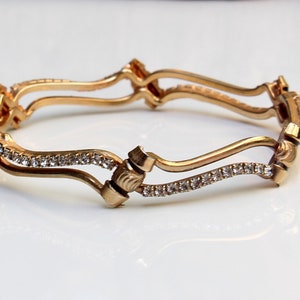 May include: A gold bangle bracelet with a wavy design and a row of clear rhinestones.