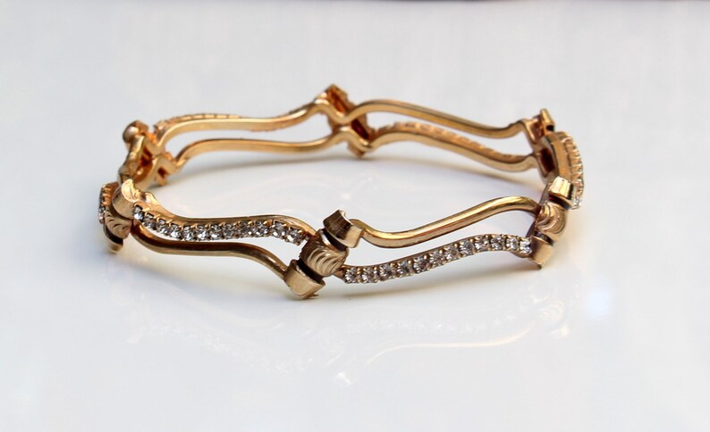 May include: A gold bangle bracelet with a wavy design and a row of clear rhinestones.