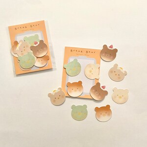 May include: A set of 10 colourful stickers featuring cartoon bears with different expressions. The stickers are shaped like bears and have a variety of designs, including a bear with a slice of bread on its head, a bear with a heart on its chest, and a bear with a slice of bread on its head. The stickers are perfect for adding a touch of whimsy to your planner, journal, or laptop.