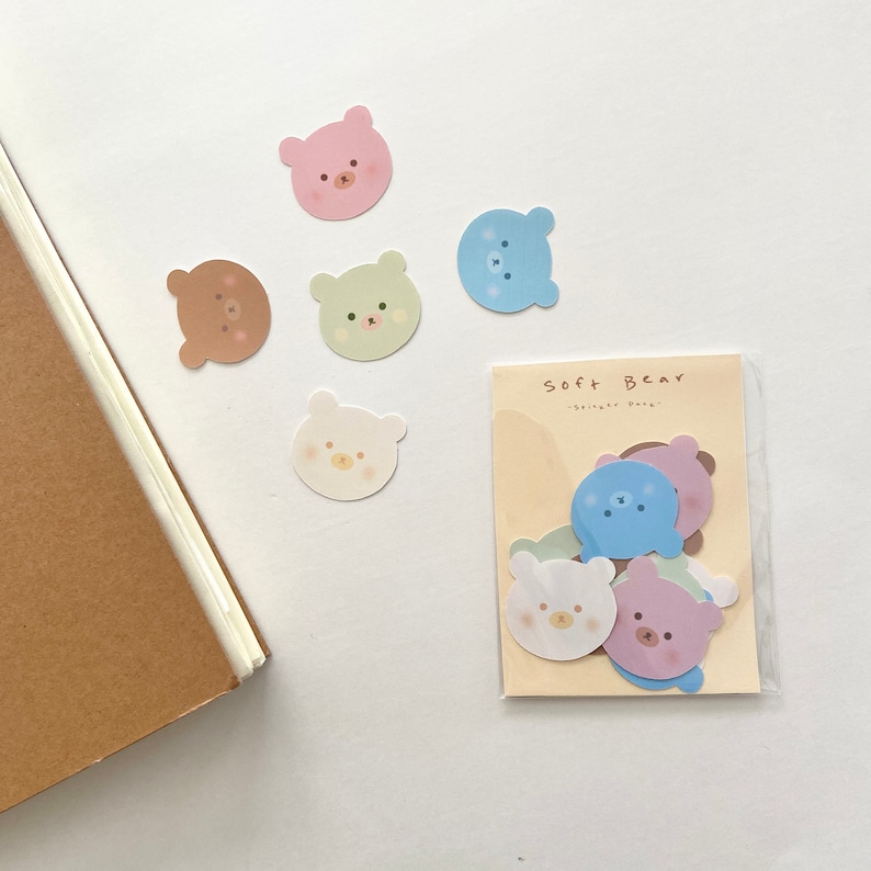 以下が含まれることがあります： 「Soft Bear」という文字が印刷された、カラフルなクマのステッカーのシート。ステッカーはピンク、ブルー、グリーン、ブラウンなど、さまざまな色があります。
