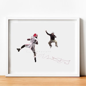 May include: A white framed print of a black and white illustration of a football player in mid-air with a coach jumping in the background. The player is wearing a white jersey with the number 5 on it. The coach is wearing a brown jacket and khaki pants. The print has a red signature in the bottom right corner.