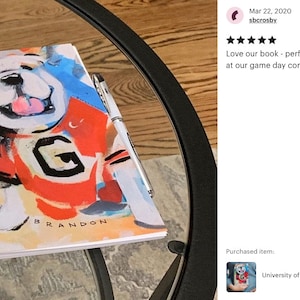K&ouml;nnte beinhalten: Ein spiralgebundenes Notizbuch mit einer farbenfrohen Illustration eines Bulldogs, der ein rot-blaues Trikot mit einem wei&szlig;en "G" auf der Vorderseite tr&auml;gt. Der Text "BRANDON" ist unter dem Bulldoggen gedruckt.