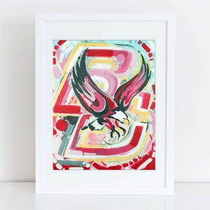 May include: Abstract art print in a white frame. The artwork features a stylized eagle with red and black wings, set against a colorful background of red, yellow, and pink brushstrokes. The print is signed.