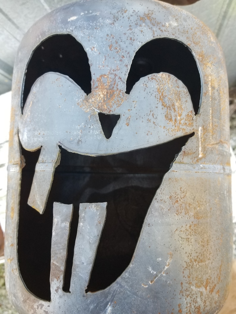 Op de afbeelding: Een roestige metalen propaantank met een gesneden jack-o'-lantern gezicht. Het gezicht heeft twee grote ogen, een kleine neus en een brede, tanden grijns.