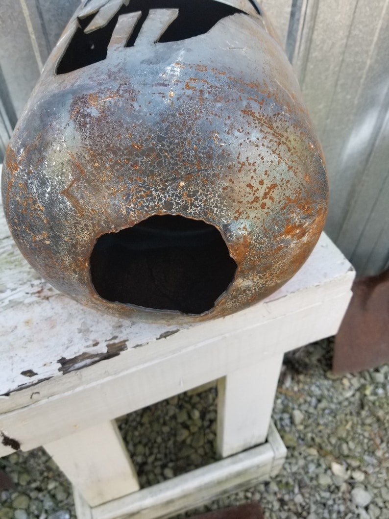 Op de afbeelding: Een roestige metalen propaantank met een groot gat aan de zijkant. De tank staat op een witte houten kruk.