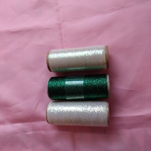 May include: Three spools of iridescent thread, one white, one green, and one iridescent white.