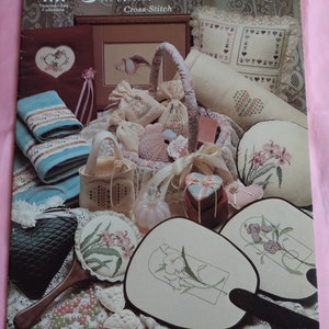 May include: Cross-stitch pattern book featuring a variety of lavender and old lace themed designs, including a pillow, a fan, a sachet, and a towel. The book cover features the text "Lavender and Old Lace Cross-Stitch" and "VAC 08".