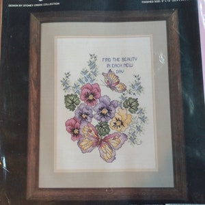 May include: Counted cross stitch pattern featuring a butterfly and flowers with the text "Find the beauty in each new day". The pattern is 22.9 cm by 30.5 cm.