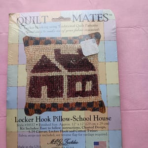 May include: A brown and beige pillow with a red and white house design. The pillow is made using a locker hook technique. The packaging includes instructions, a charted design, canvas, locker hook, and cotton twine. The finished size is 12 inches by 12 inches.  The product is made in the USA.