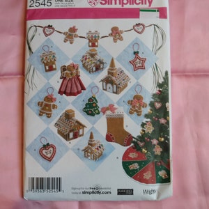 May include: Simplicity sewing pattern featuring Christmas gingerbread house and ornament designs. The pattern includes various gingerbread house shapes, gingerbread people, and a Christmas stocking. The pattern is labeled "2545" and includes the text "ONE SIZE".