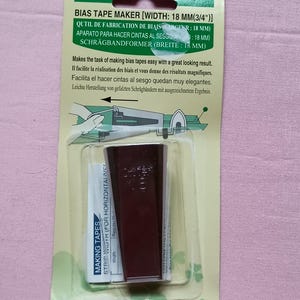 May include: A dark maroon Clover brand bias tape maker tool with a width of 18 mm or 3/4 inches, packaged in a green and cream cardboard backing with instructions and a diagram showing the tool in use for creating fabric bias strips.