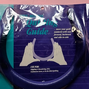 May include: A dark blue quilting guide in a plastic package. The guide is a curved handle shape. Text on the package reads "Quilting Guide" and "move your quilt sandwich with ease". The guide is used for stippling, meandering, echo, continuous curve, or in-the-ditch quilting.