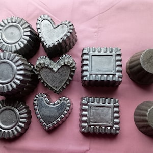 May include: A set of nine silver-colored metal molds for baking. The molds are shaped like hearts, circles, and squares.