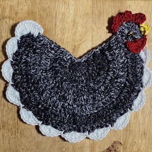 Pode incluir: Um porta-copos ou aplique de croch&ecirc; em formato de galinha com corpo em fio mesclado cinza escuro e preto, crista e barbelas vermelho vivo, bico amarelo e uma borda decorativa branca em vieira contornando todo o per&iacute;metro da pe&ccedil;a.