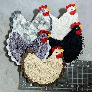 May include: Five handmade crochet chicken-shaped pot holders in various colors. The pot holders feature red combs and yellow beaks. Colors include white, black, gray, and speckled beige. Each has a scalloped edge.